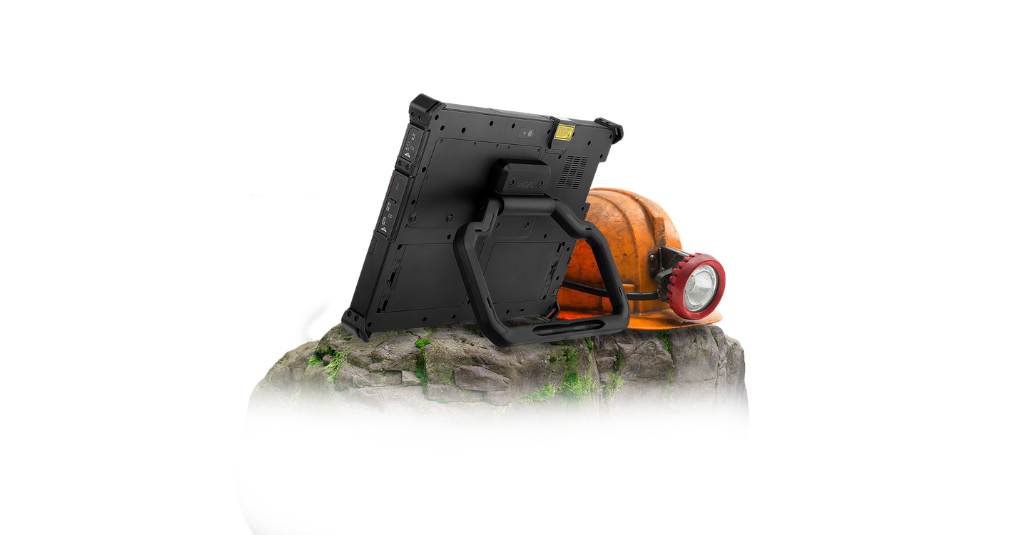 Getac G140 rugged tablet standing upright on rocky terrain using the built-in kickstand, with a mining hard hat in the background