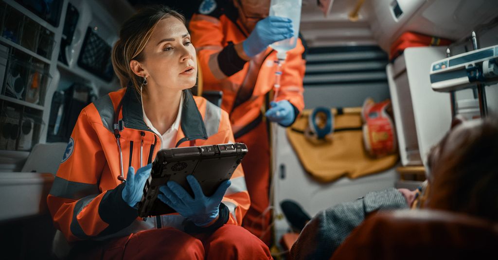 emergency service worker assessing patient, logging details on rugged tablet