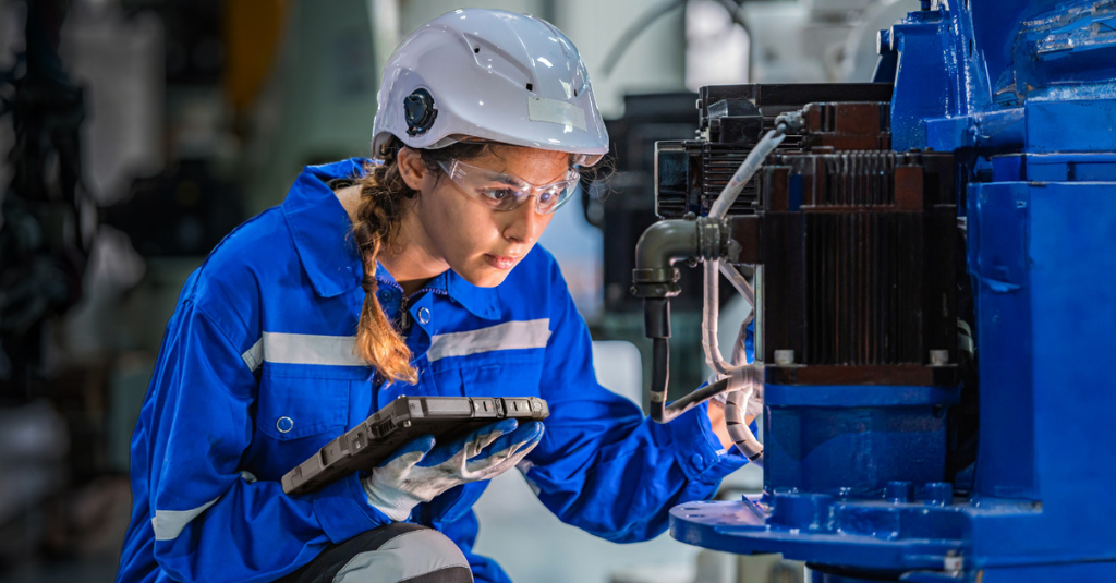 Field technician in safety gear holding a rugged tablet while inspecting industrial machinery in a plant environment