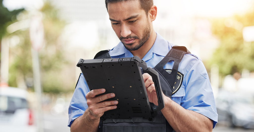 Police officer in tactical vest using a Getac G140 rugged tablet handheld during an outdoor patrol