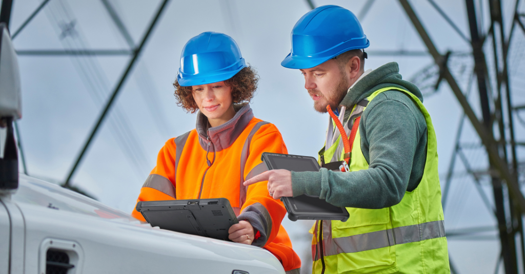 Two utility workers refer to a Getac rugged tablet while being out in the field for inspections.