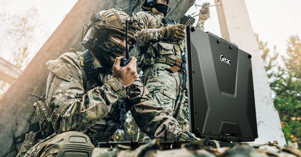 Soldiers using a Getac rugged computer during a field operation, demonstrating mission-ready durability and customized military COTS-based technology for secure, real-time communication.
