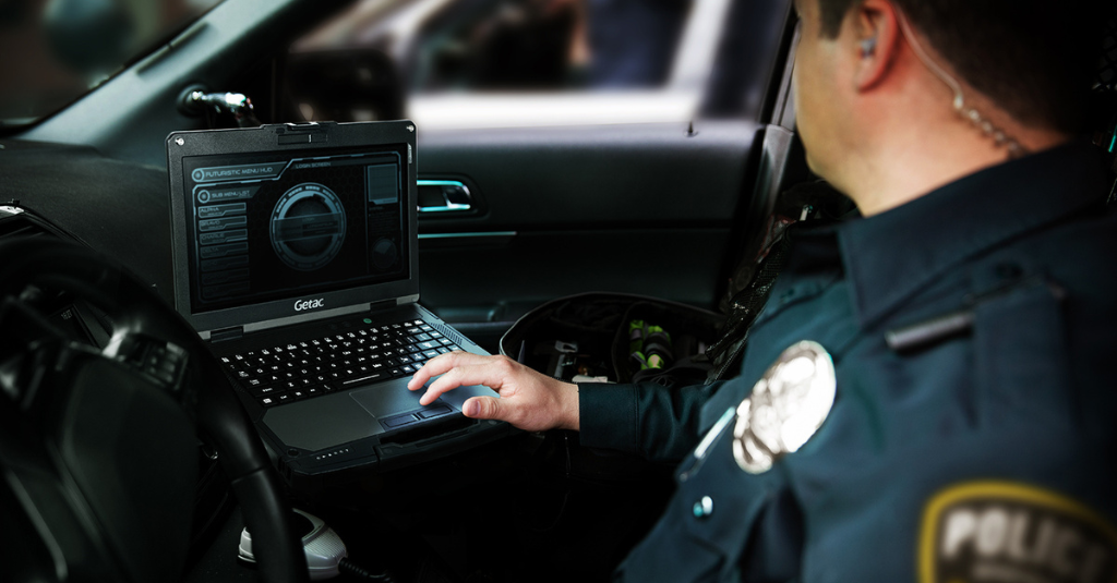 Police officer using a Getac rugged laptop inside a patrol vehicle to access real-time data and dispatch information during field operations.