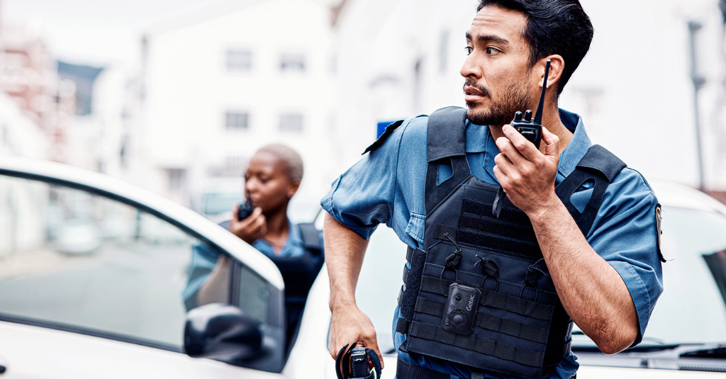 Public safety officers equipped with Getac body-worn cameras and rugged devices coordinating in the field beside a patrol vehicle.